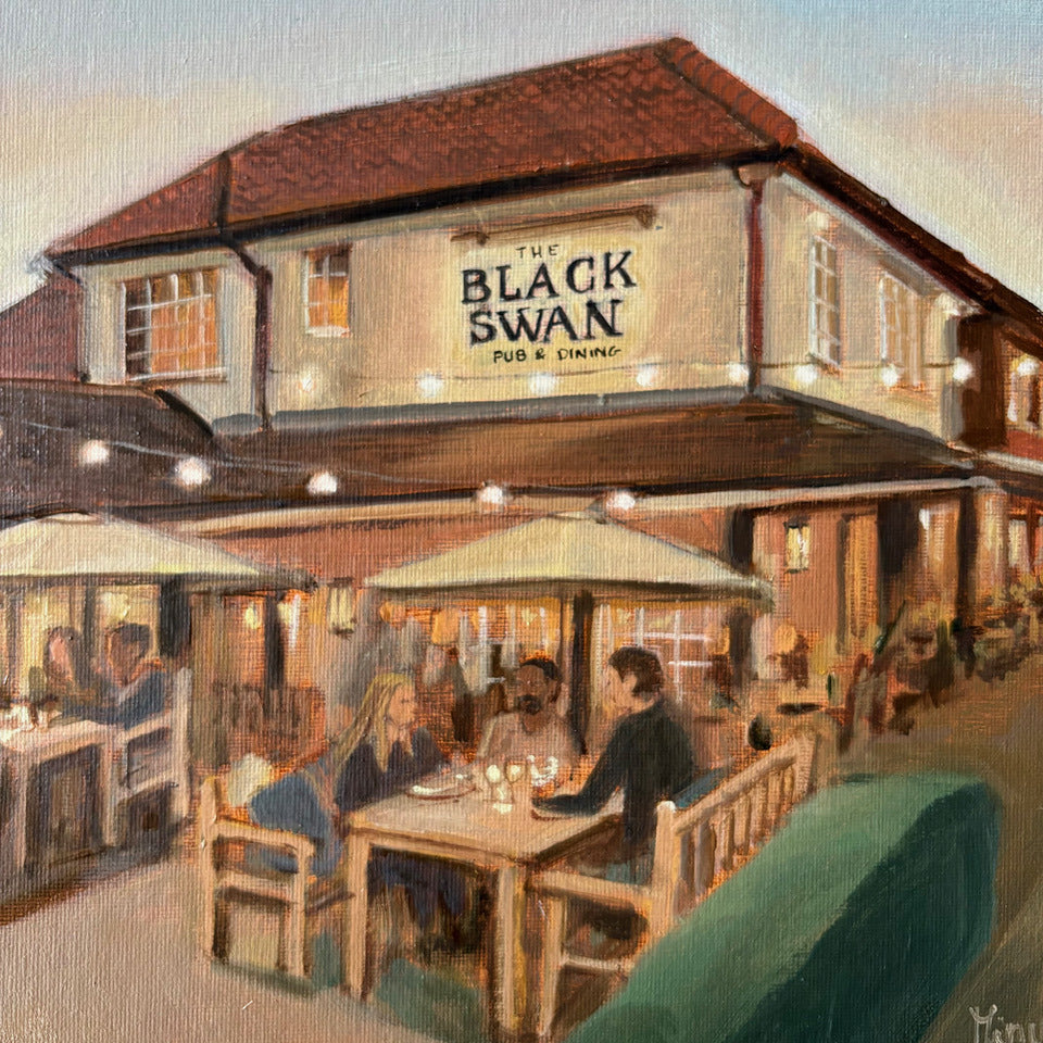 Original oil painting of The Black Swan pub and dining rooms at dusk by Minuca Sostres, with festoon lights, parasols and diners on the terrace.