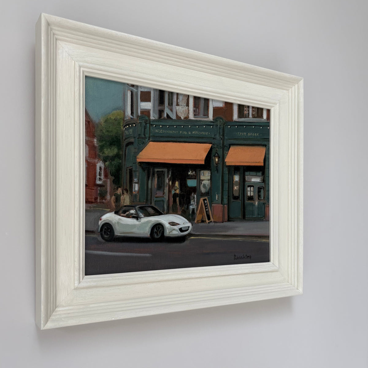 Framed oil painting of Independent Pub & Kitchen by Minuca Sostres, showing its dark green façade, orange awnings and a white convertible outside.
