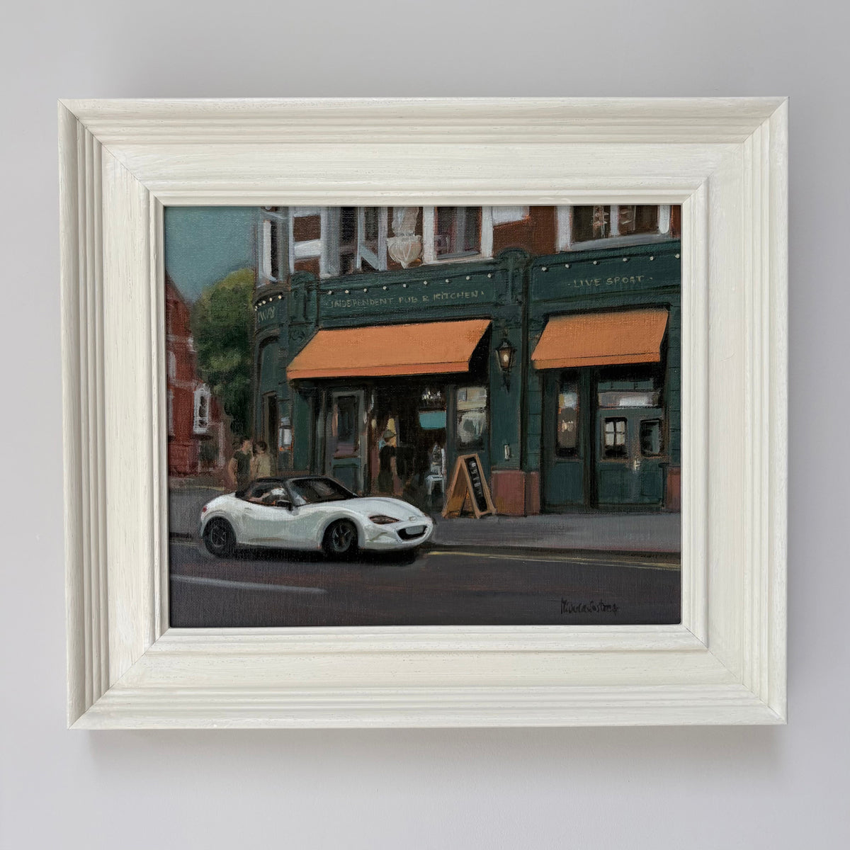 Framed oil painting of Independent Pub & Kitchen by Minuca Sostres, showing its dark green façade, orange awnings and a white convertible outside.