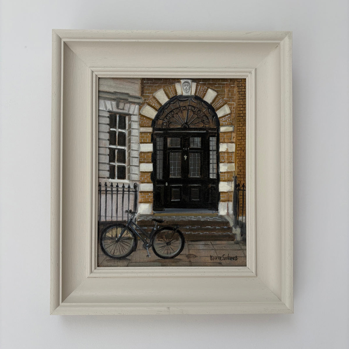Framed oil painting of a London doorway by Minuca Sostres, showing black double doors beneath a brick arch and a bicycle parked outside.