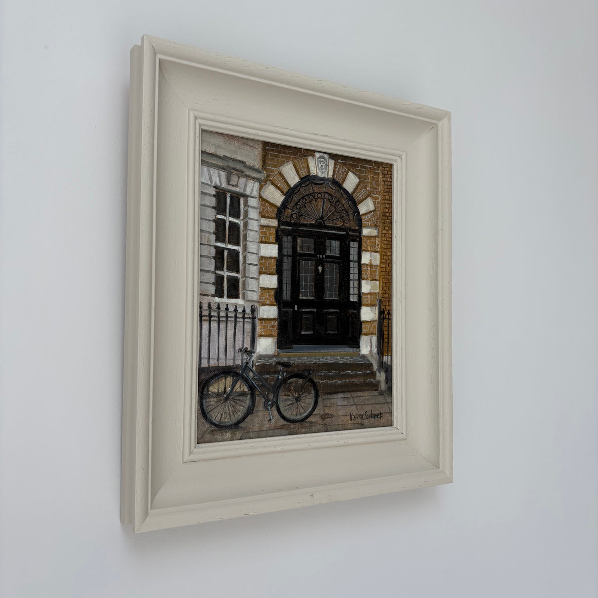 Framed oil painting of a London doorway by Minuca Sostres, showing black double doors beneath a brick arch and a bicycle parked outside.