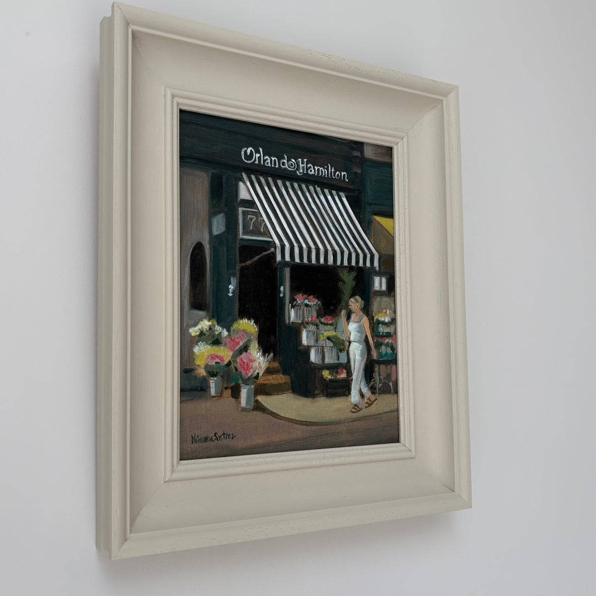 Framed oil painting of Orlando Hamilton flower shop by Minuca Sostres, showing bouquets beneath a striped awning and a woman walking past.